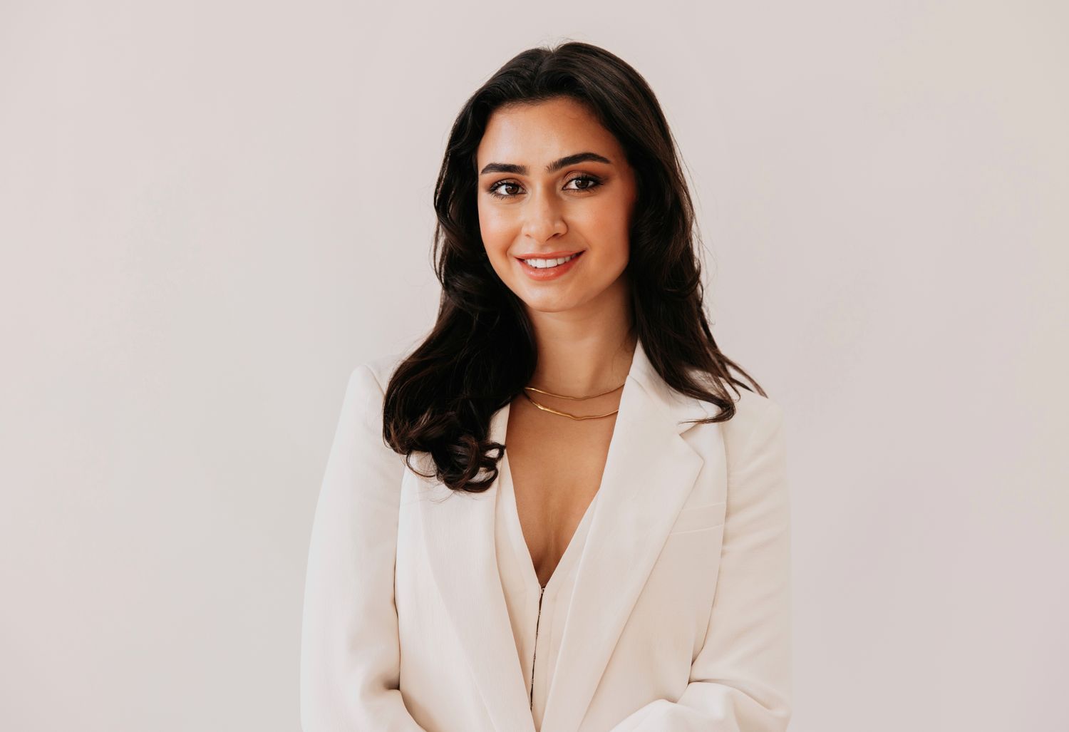 Woman in white suit sitting on stool.