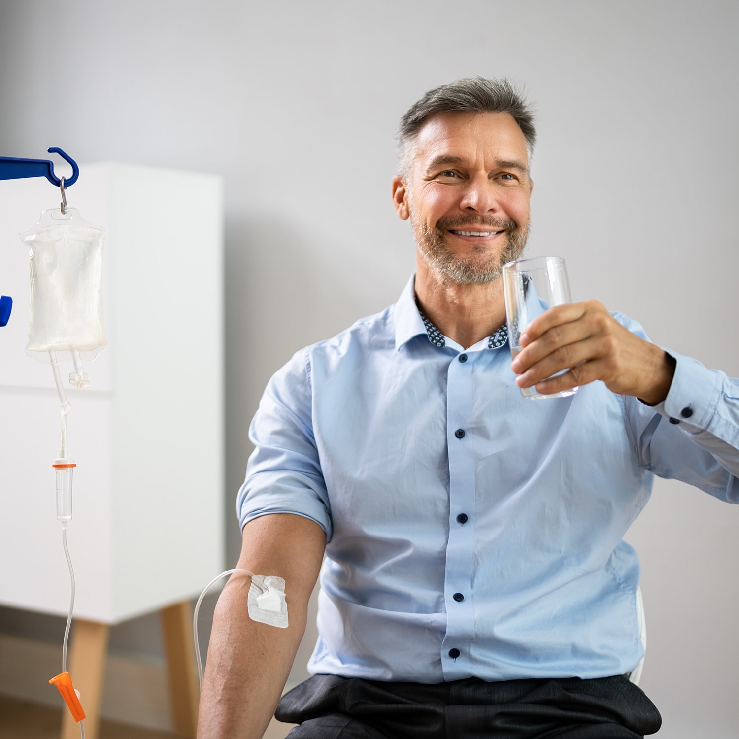Man receiving IV treatment while smiling and holding water.
