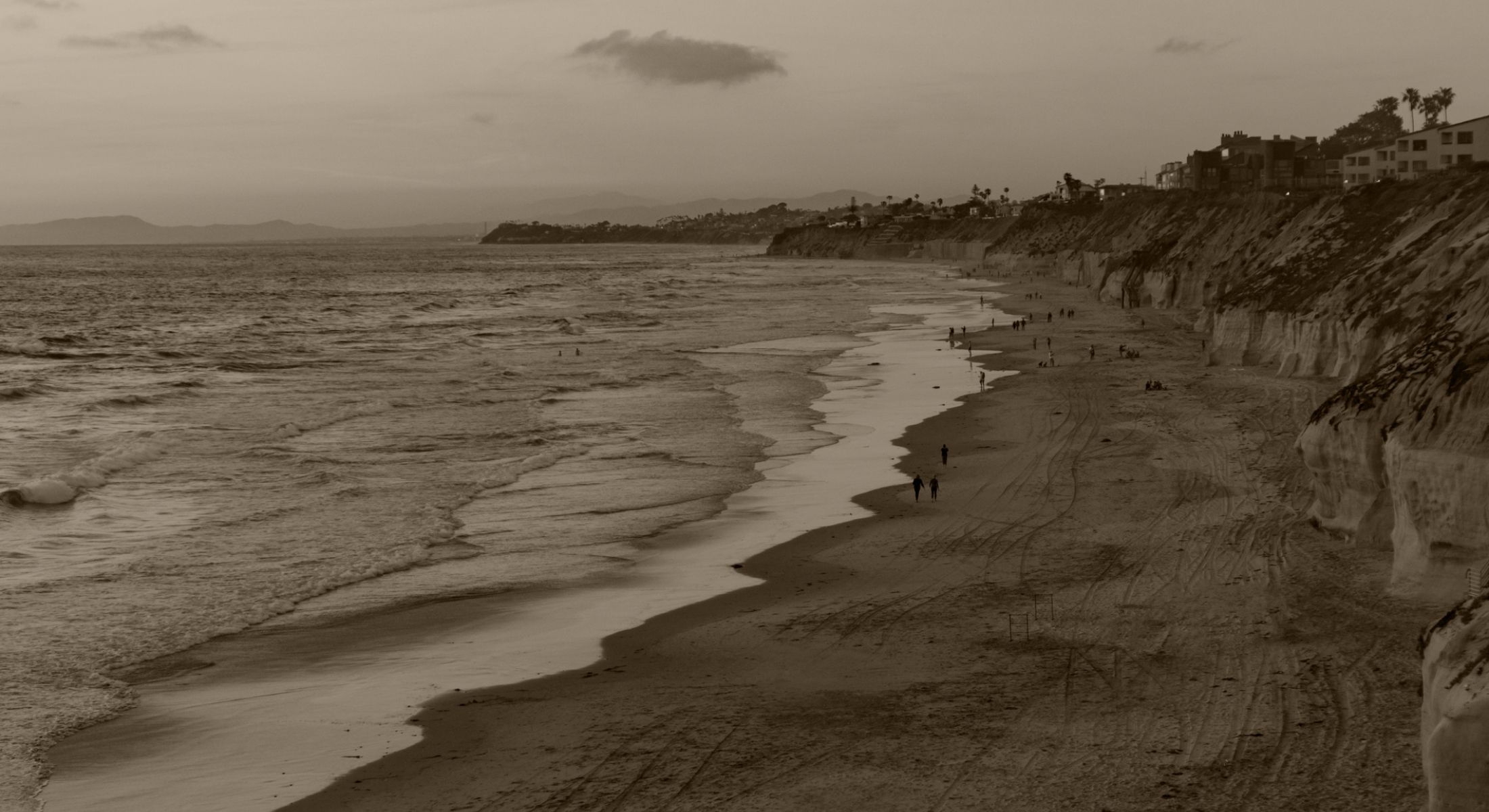 Secluded beach with people walking at twilight.